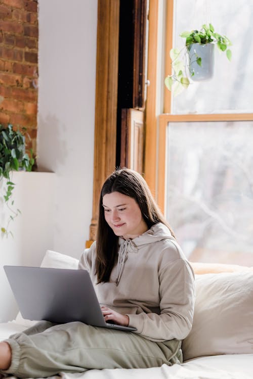 Free Smiling young female freelancer in casual clothes using laptop while sitting on sofa and working remotely from home Stock Photo