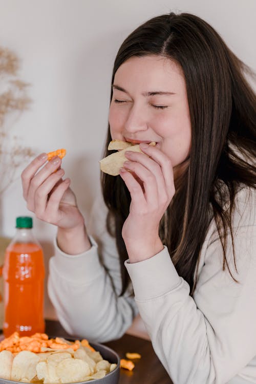 Hungry young lady enjoying potato chips at home