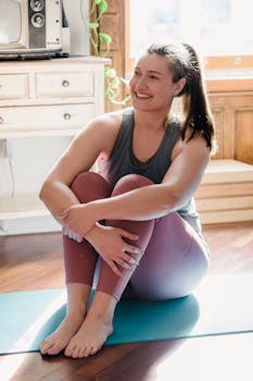 A woman sitting on a yoga mat at home, enjoying sunlight and relaxation.