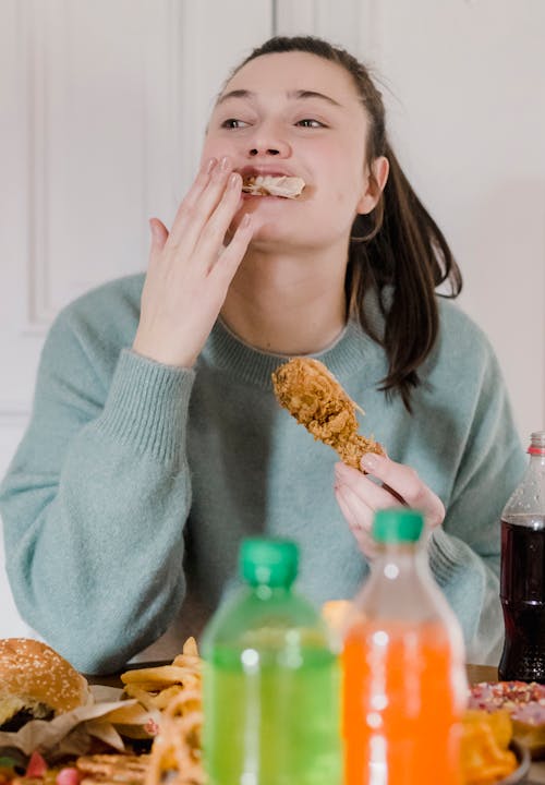 Cheerful woman eating fried chicken at table with lemonade
