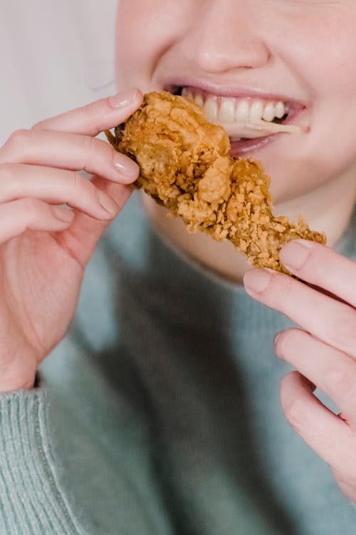 Crop anonymous happy female eating and enjoying spicy tasty chicken in hands and smiling