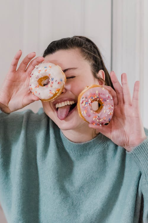 Cheerful woman with tongue out showing sweet doughnuts in glaze