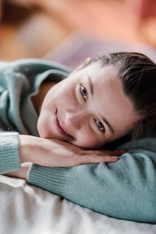 Positive crop female with dark hair smiling and looking at camera on soft bed on blurred background
