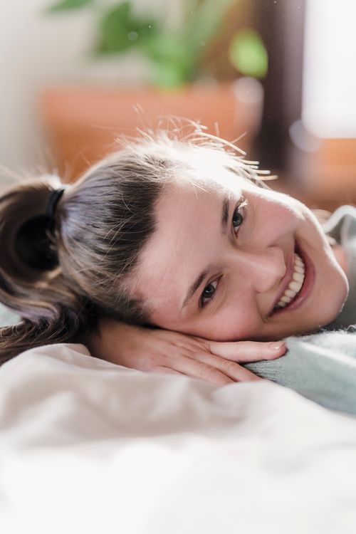 Free Glad female relaxing and smiling on bed on blurred background of apartment in daytime Stock Photo