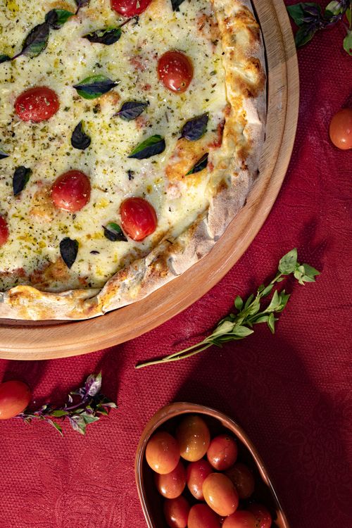 Free Delicious Italian pizza with cherry tomatoes and herbs on a rustic wooden platter. Stock Photo