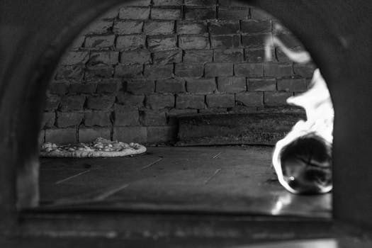 Black and white image of a traditional brick oven with wood fire and baking bread.