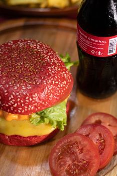 Close-up of a vibrant red bun burger with cheese and lettuce, served with a soda.