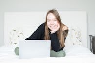 Woman in Black Long Sleeve Shirt Sitting on White Bed