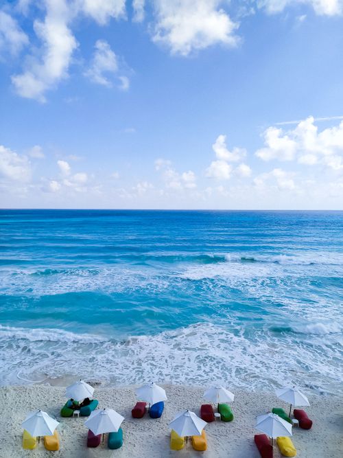 Free A vibrant aerial view of colorful beach chairs and umbrellas on Cancún shore with blue ocean waves. Stock Photo