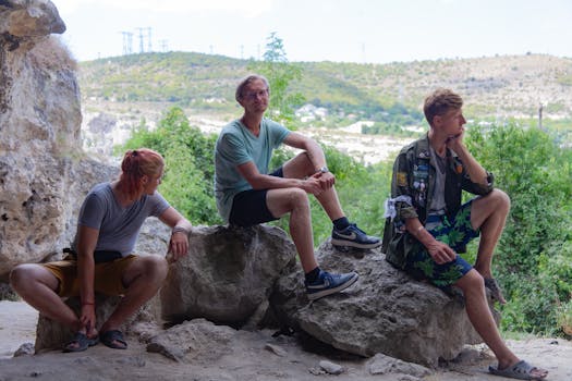 Three young men sitting on rocks in a natural setting, enjoying an outdoor moment together.