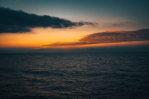 Free Tranquil ocean scene at sunset with vibrant sky and clouds showcasing nature's beauty. Stock Photo