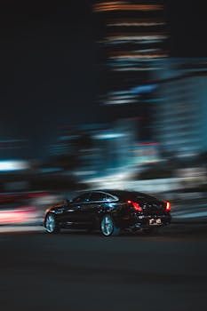 Black sedan in motion, panning shot at night in urban Jakarta setting.