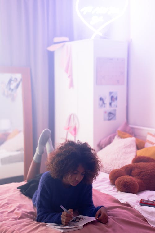 Teenage Girl Lying on Bed While Writing on a Diary