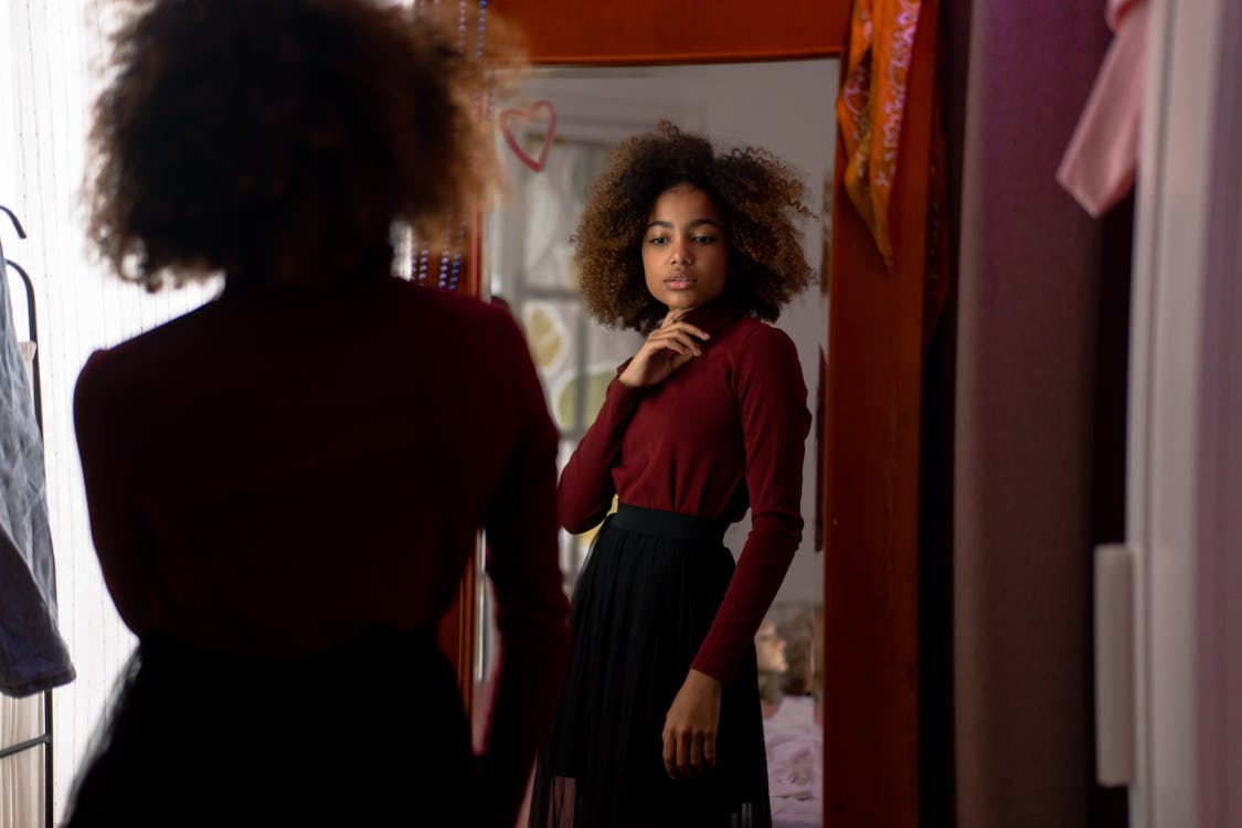 A Woman in Red Long Sleeve Shirt Looking at the Mirror