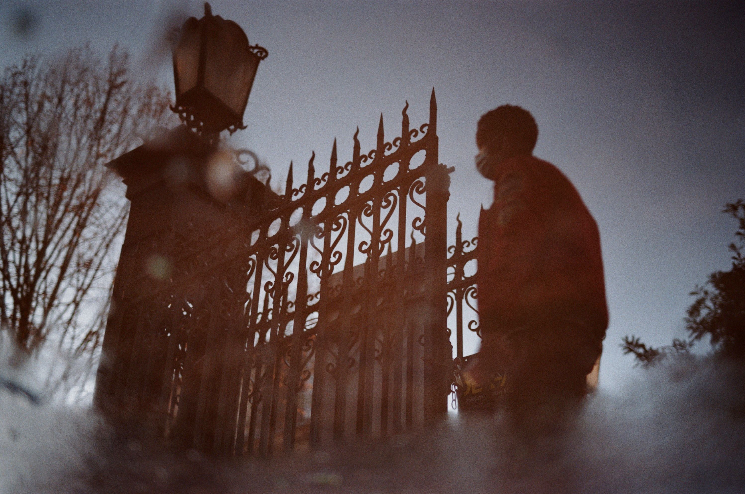 Silhouette of a person standing by a decorative iron gate at dusk, creating a mysterious atmosphere.