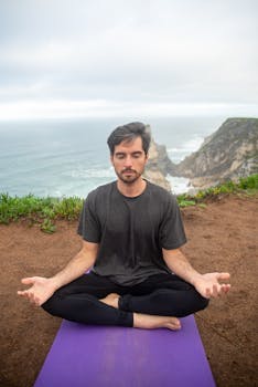 Man meditating on a cliff in Portugal, overlooking the ocean, promoting relaxation and wellness.