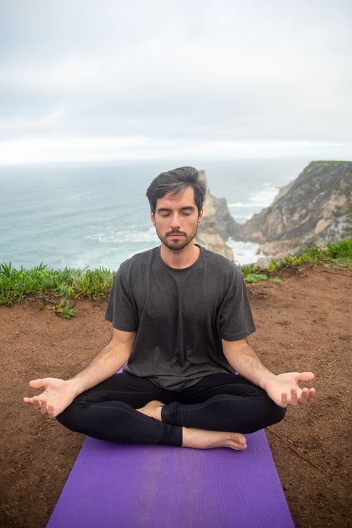 Free Man meditating on a cliff in Portugal, overlooking the ocean, promoting relaxation and wellness. Stock Photo