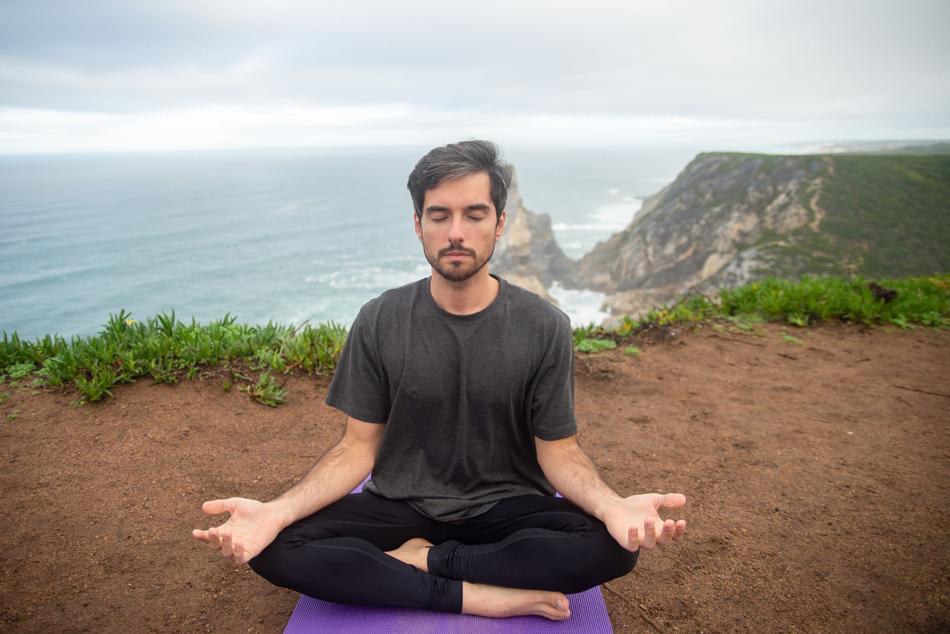 A man meditates on a cliff in Portugal, embracing calmness and nature.