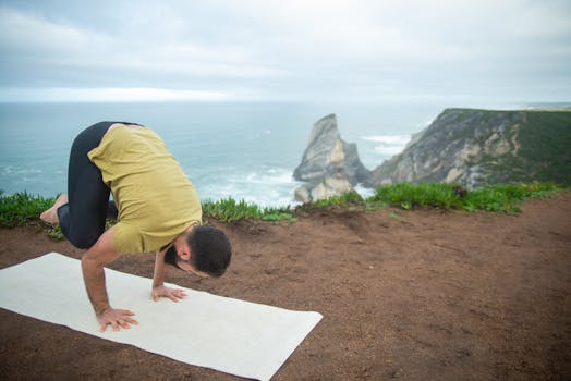 A man balances in a yoga pose by the ocean cliffs in Portugal, showcasing fitness and tranquility.
