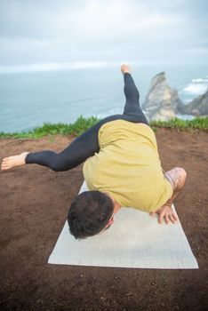 Man in a green shirt doing yoga on a cliff overlooking the sea in Portugal.