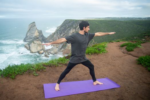 A man performs a yoga pose on a cliff overlooking the sea in Portugal.