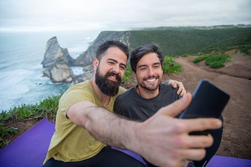 Free Two friends smile and take a selfie with scenic cliffs and ocean in the background in Portugal. Stock Photo