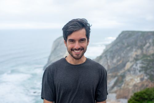 Free A man smiles on picturesque Portuguese coastal cliffs under a cloudy sky, creating a cheerful and calm atmosphere. Stock Photo