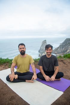 Two men practicing yoga at a cliff edge with a stunning ocean view.