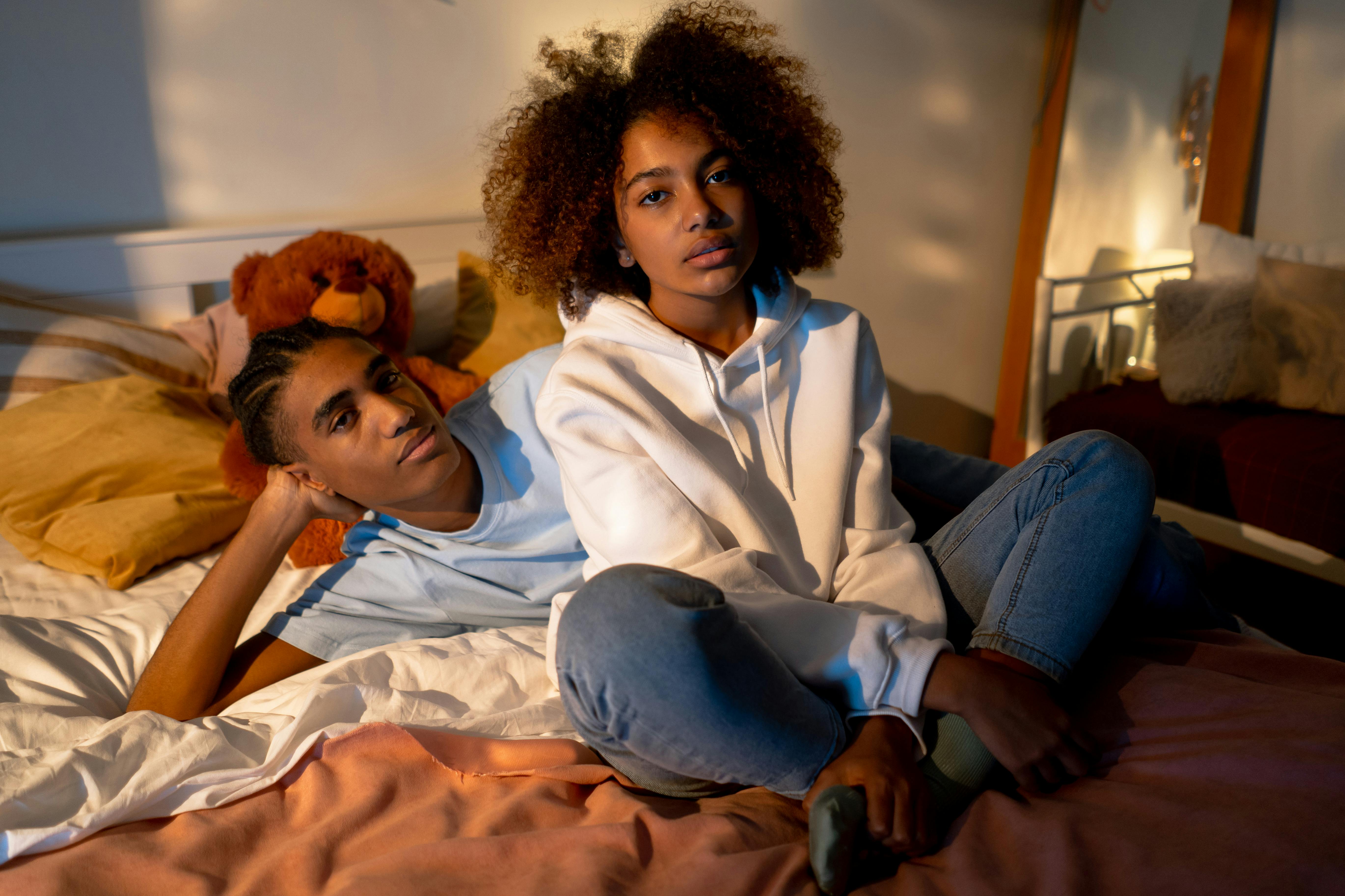 a girl sitting and a boy lying on bed