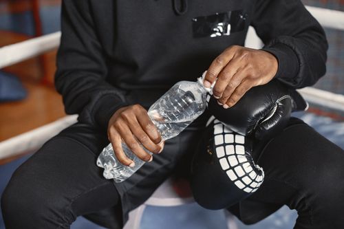 Free A boxer in black outfit holding a water bottle during a break indoors. Stock Photo