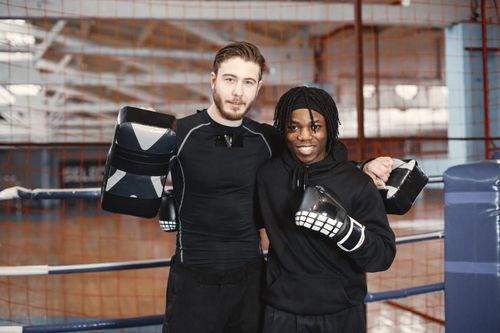 Free Two smiling boxers pose in a gym boxing ring, wearing gear, trainers, and gloves. Stock Photo
