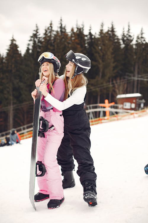 Two Women in Sports Clothing Posing with a Snowboard 