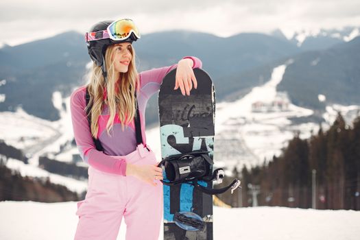 Female snowboarder posing with snowboard in a snowy mountain resort, showcasing winter sport fashion.