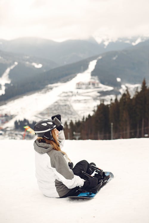 Woman Sitting on the Slope with a Snowboard next to Her 