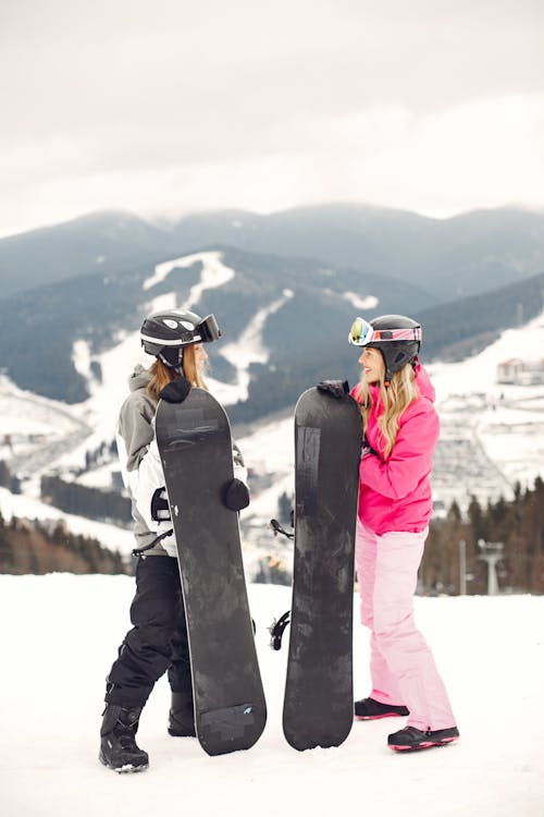 Two Women Standing with the Snowboards in the Mountains 