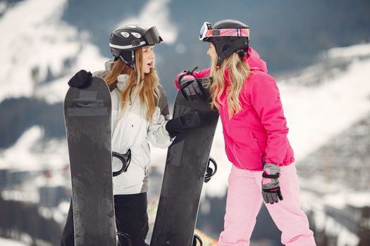 Two women snowboarders in vibrant gear sharing a moment on a snowy mountain slope.