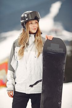 Smiling woman in winter gear and helmet holding snowboard on snowy mountain slope.