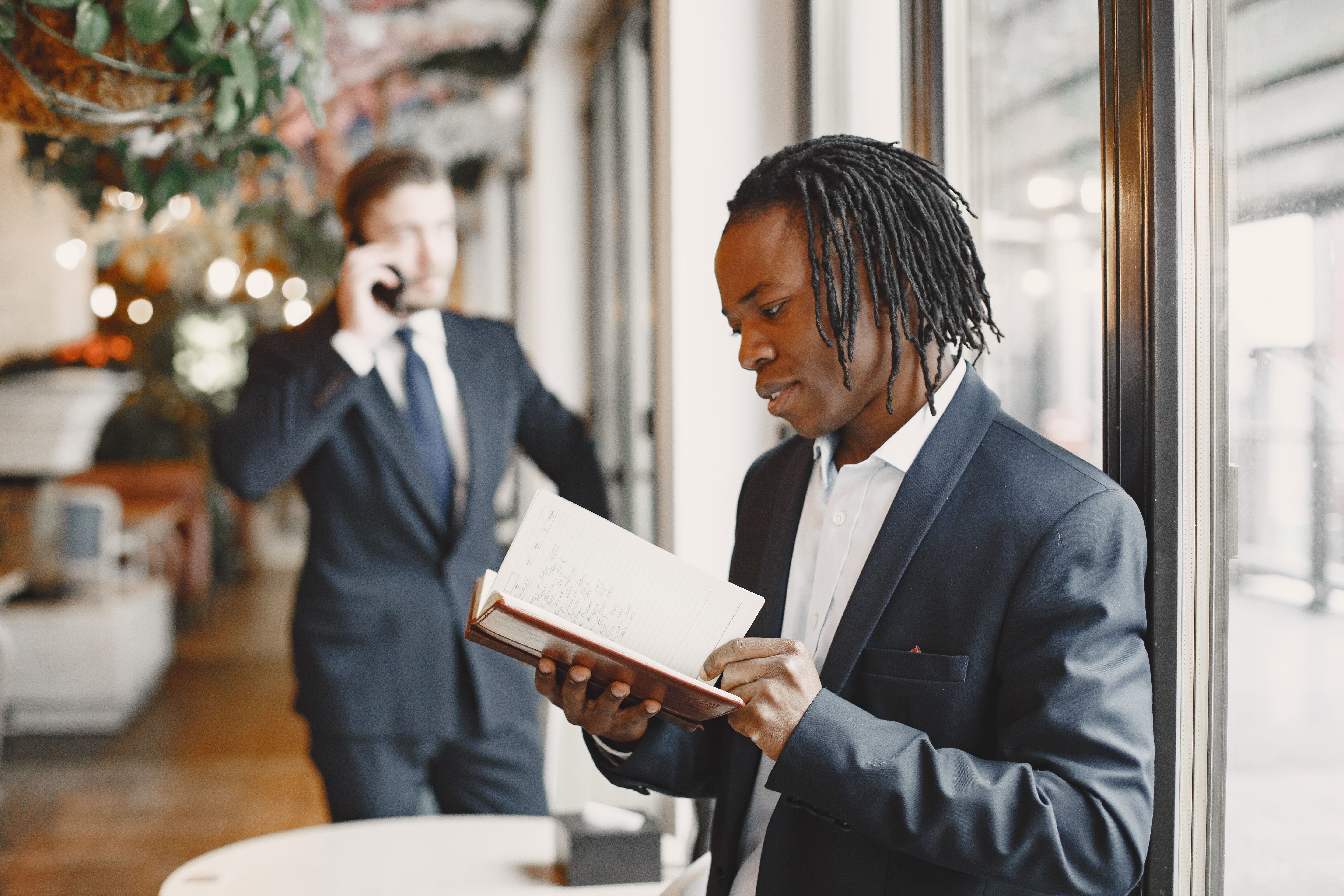 Professional man in a suit reading a book near glass windows, corporate office interior.