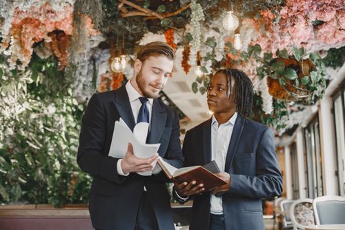 Free Two businessmen in suits review documents amidst lush interior decor with hanging plants. Stock Photo