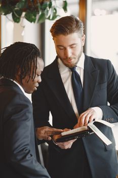Two businessmen in suits discussing strategy with an open book indoors.