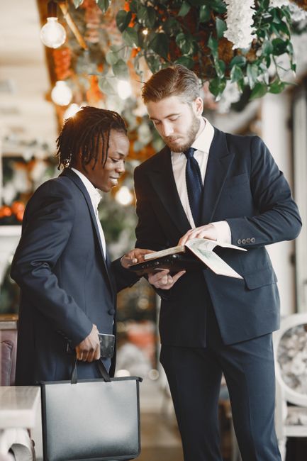 Two businessmen in suits discussing plans indoors with a briefcase and tablet. Two businessmen in suits discussing plans indoors with a briefcase and tablet.