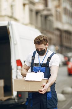 Delivery worker wearing face mask holding a package in urban street scene.