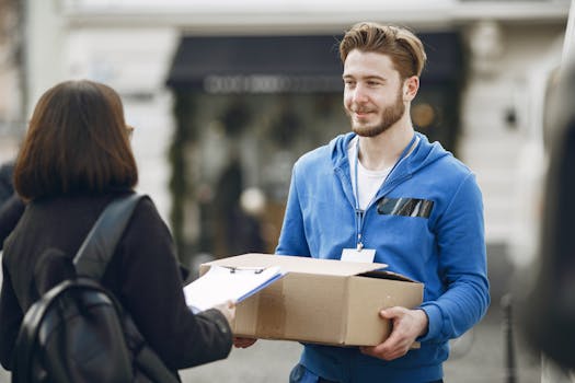 Friendly delivery person in blue hoodie gives package to customer outside. Perfect for business images.