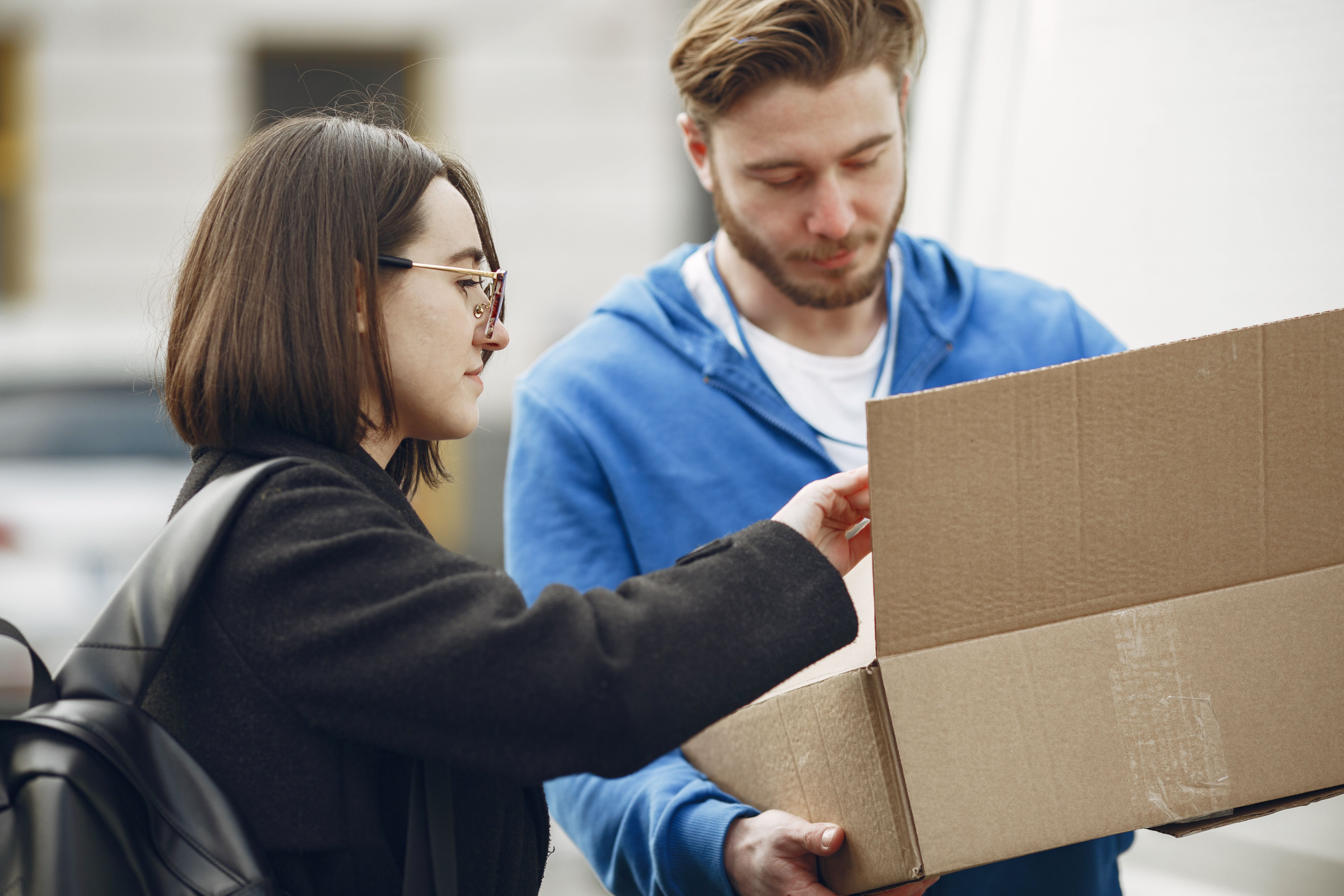 Man and woman handling a package outdoors. Urban delivery scene with cardboard box.