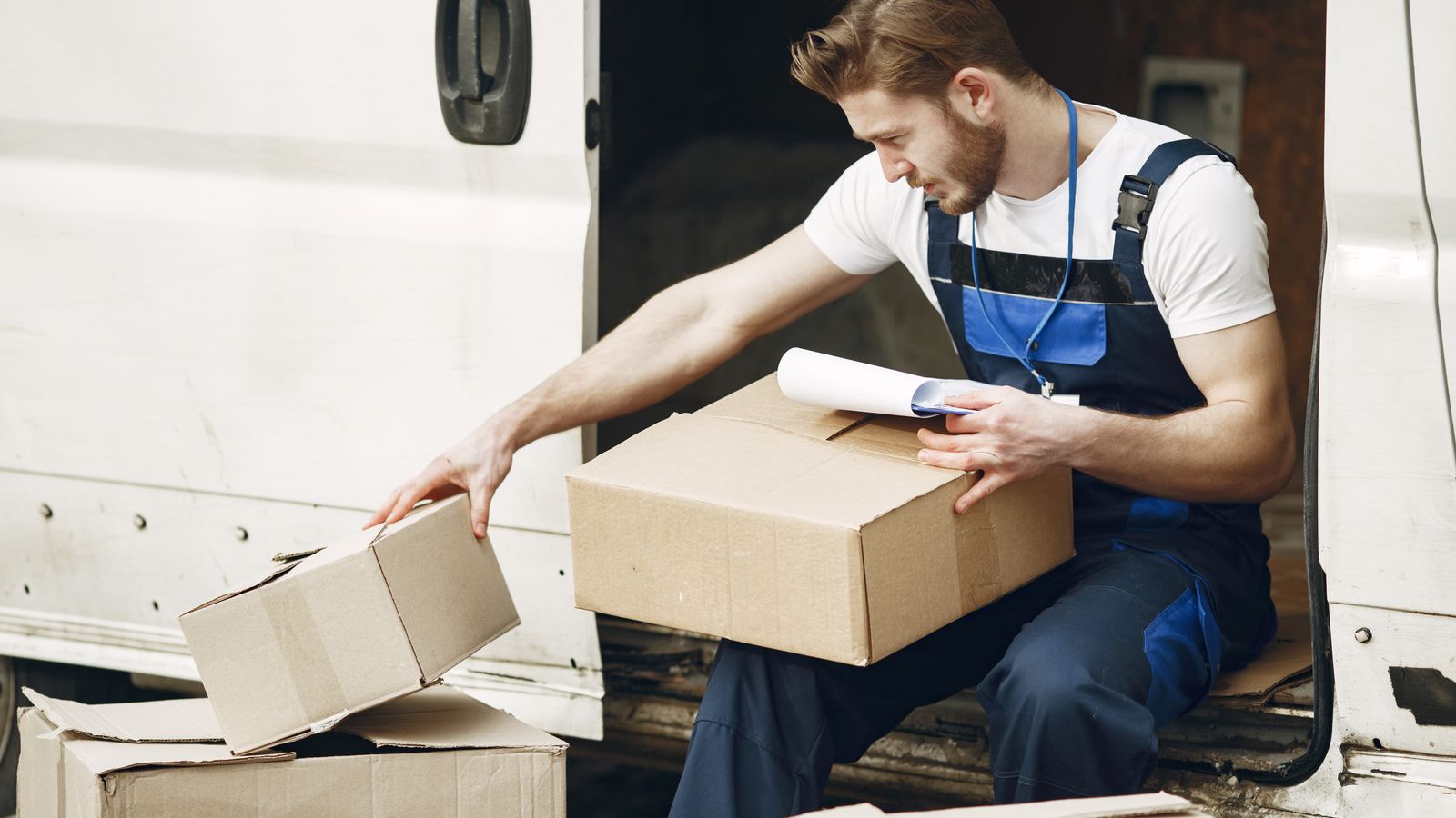 Man in uniform sorts packages by a white van, emphasizing efficient delivery service.