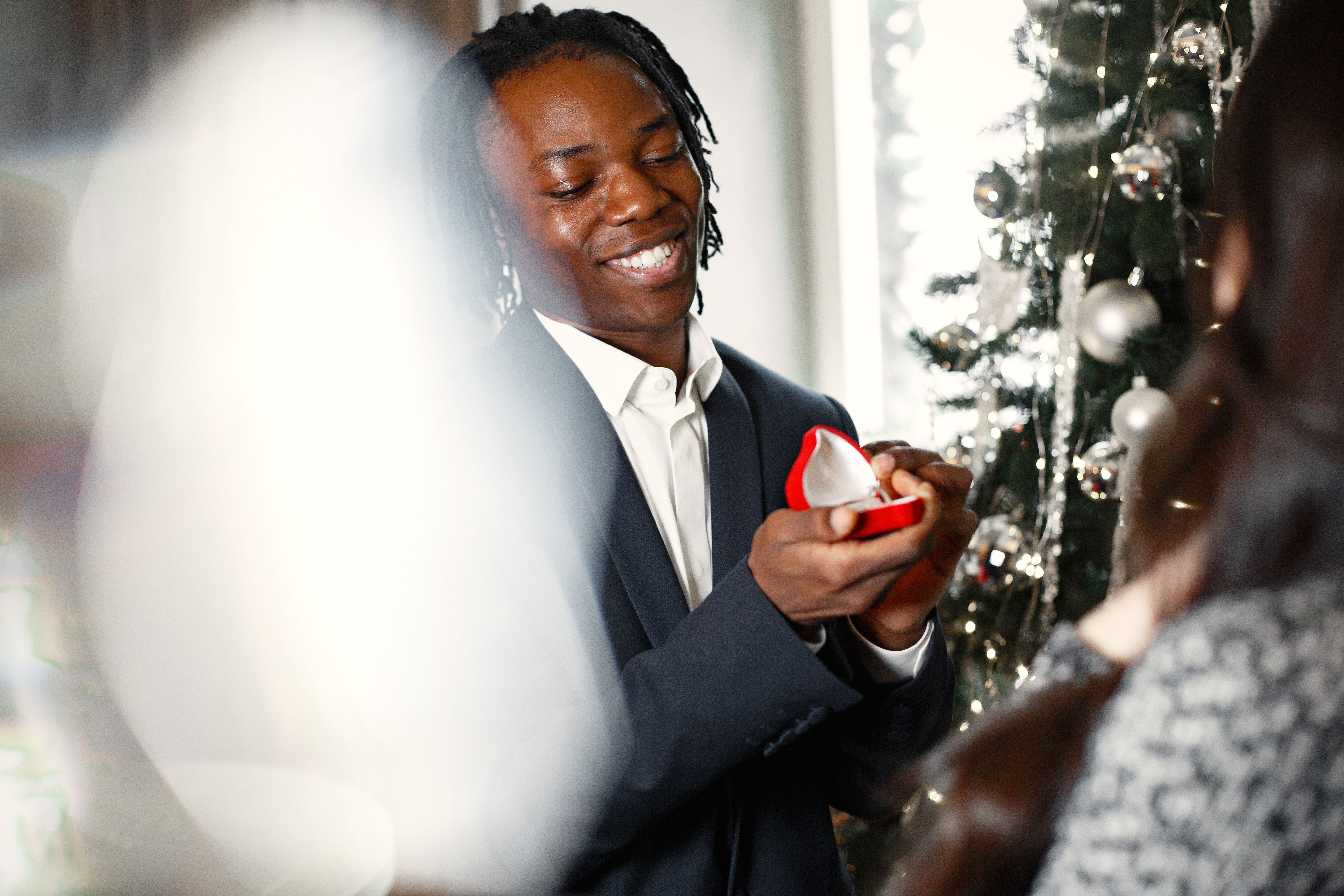 Man proposing with a ring in a festive setting with Christmas decorations and a joyful smile.