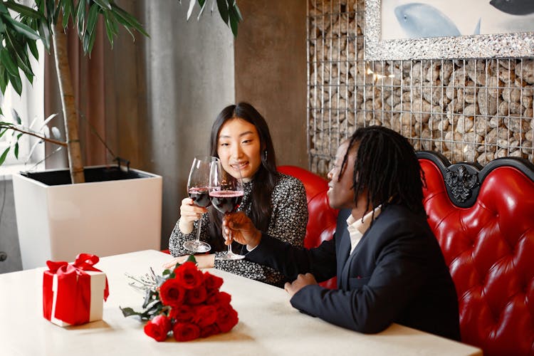 Young Man And Woman Drinking Red Wine On A Red Furniture