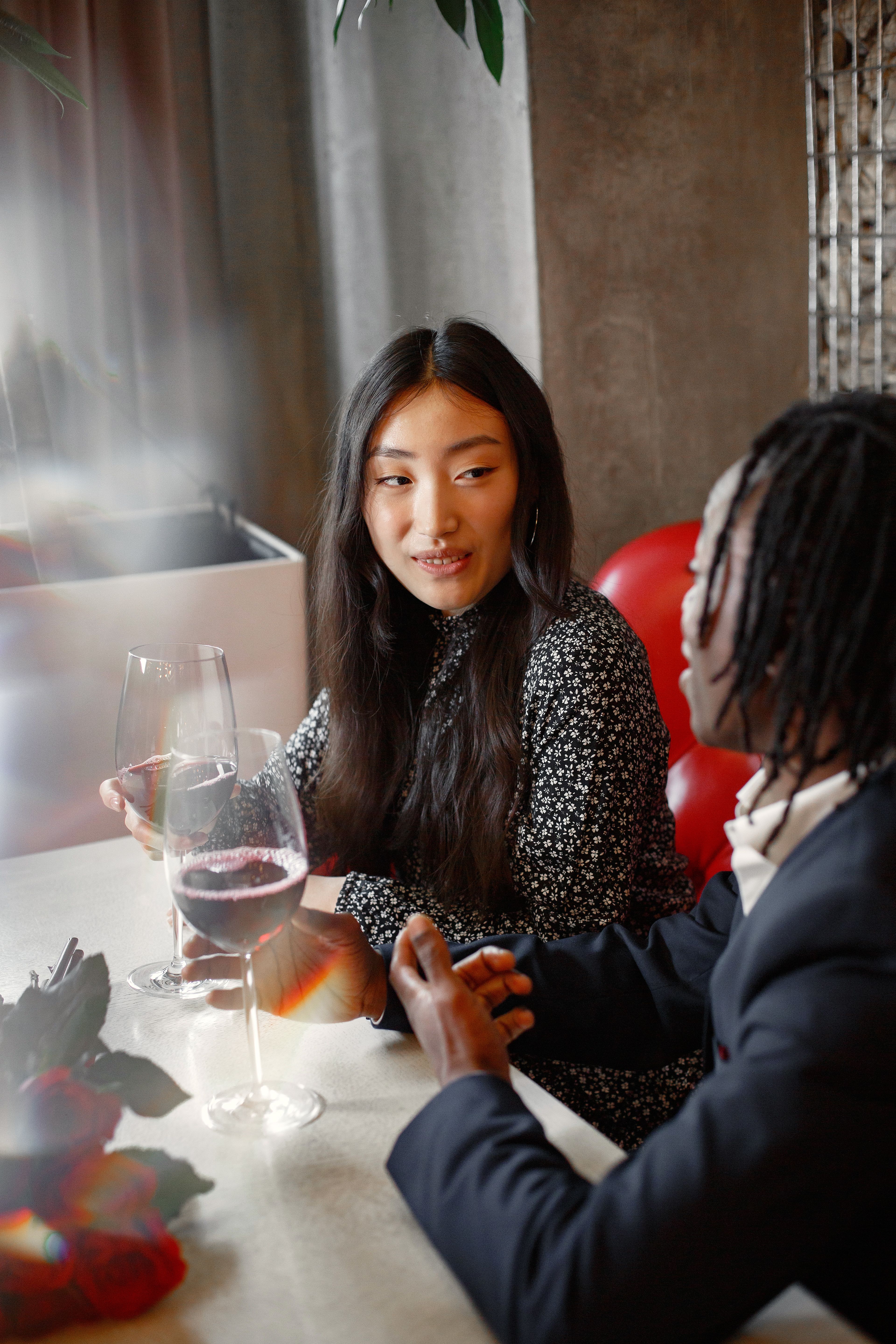 An Asian woman and a Black man enjoying a romantic dinner date with wine indoors.