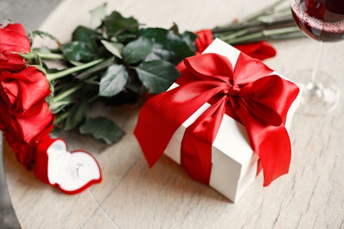 Free Gift Box with Red Ribbon beside Red Roses Stock Photo