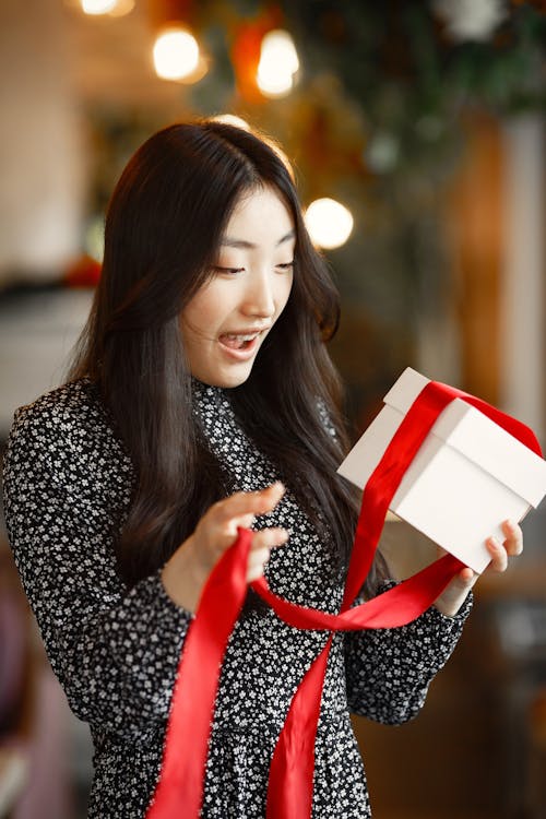 A Woman in Floral Print Dress Holding a Gift Box With Red Ribbon